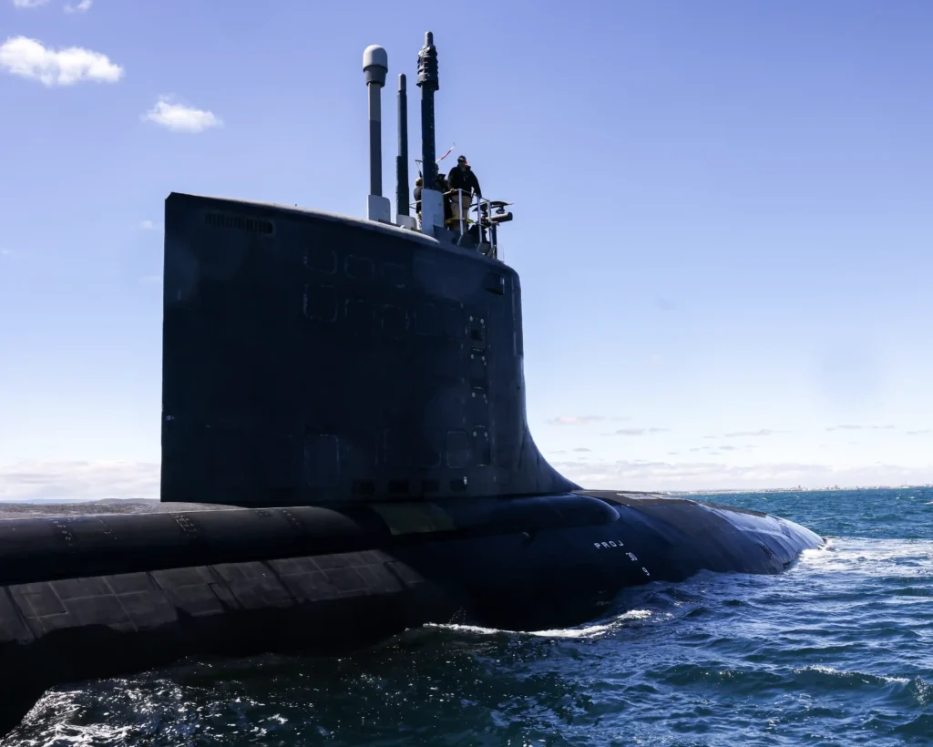 A black submarine on the ocean surface with crew members standing on the sail