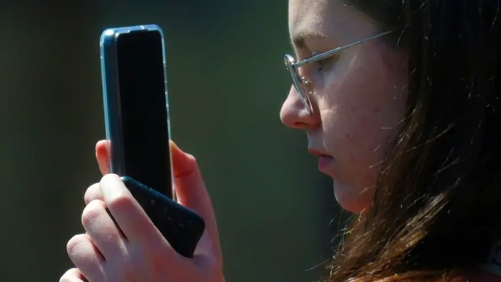 A teenager holds a glowing smartphone screen inside a house reflecting low ambient light.